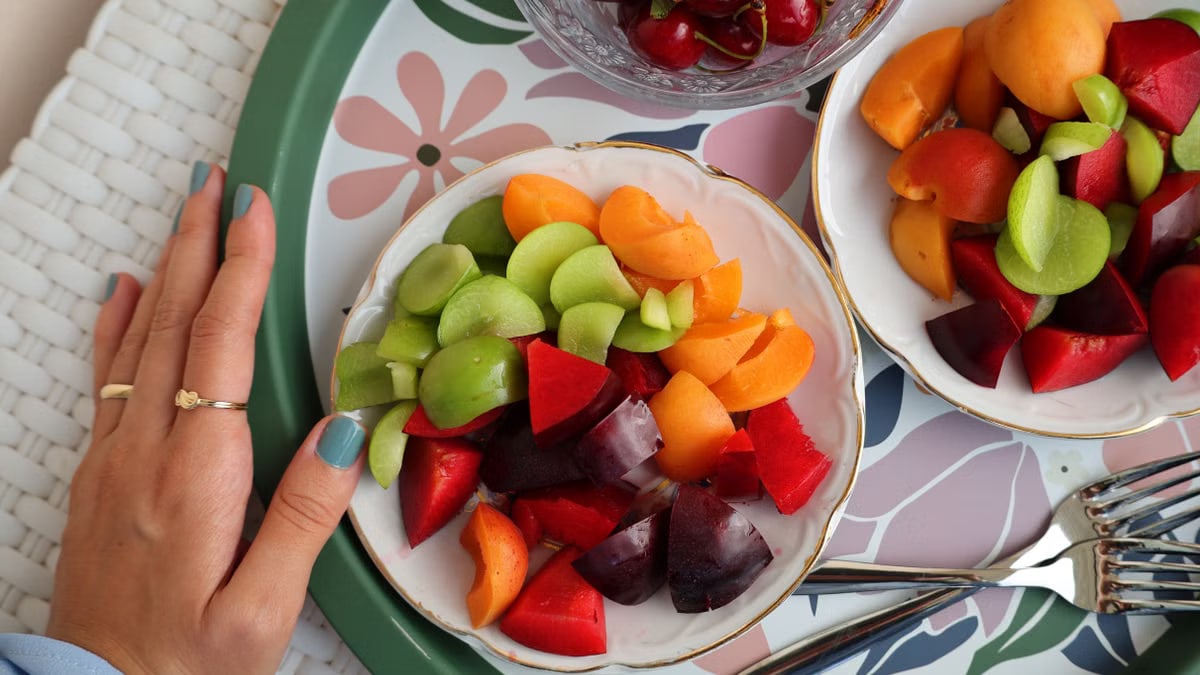 Top view of a colorful fruit platter with cherries, apricots, and plums on a decorative tray.